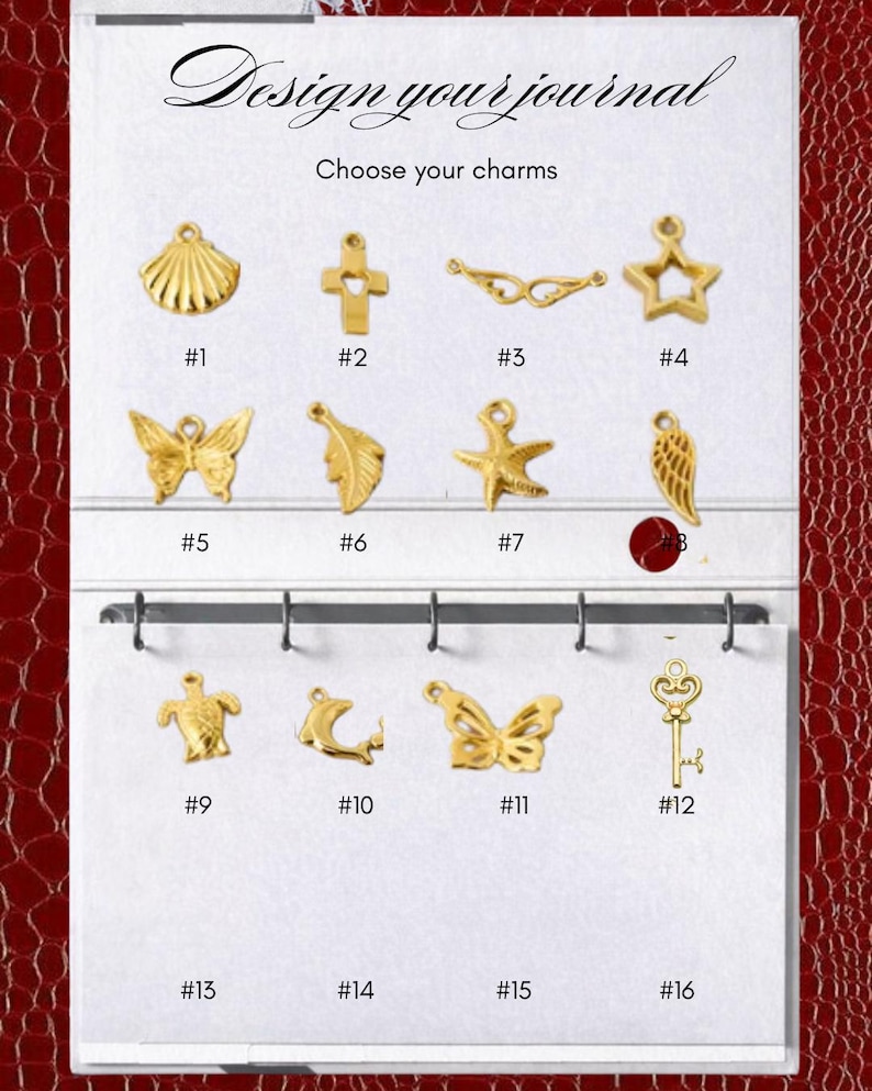 May include: A white display card with the text Design your journal and Choose your charms, featuring twelve gold-toned metal charms numbered 1 through 12. The charms include shapes like a shell, cross, wings, star, butterfly, leaf, starfish, feather, turtle, dolphin, and key.