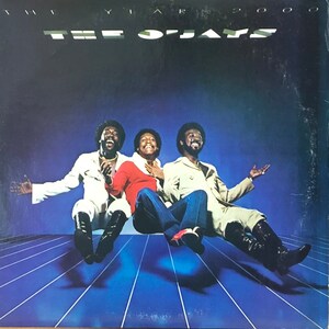 May include: The O'Jays album cover featuring three men in white, red, and beige clothing, smiling and floating in mid-air against a blue background with white stripes. The album title "The O'Jays" and "The Year 2000" are printed in white on a black background.