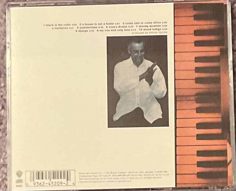 May include: A CD case with a white background and a black and white barcode. The text on the case reads: '1 black is the color 2 a house is not a home 3 come rain or come shine 4 a invitation 5 summertime 6 nica's dream 7 stormy weather 8 django 9 my one and only love 10 wood indigo produced by jimmy lovine'.