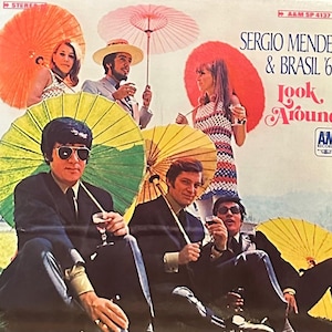 May include: A vintage vinyl record album cover featuring a group of six people, including four men and two women, holding colorful umbrellas. The album cover is titled "Sergio Mendes & Brasil '66 Look Around" with the AM Records logo in the bottom right corner.