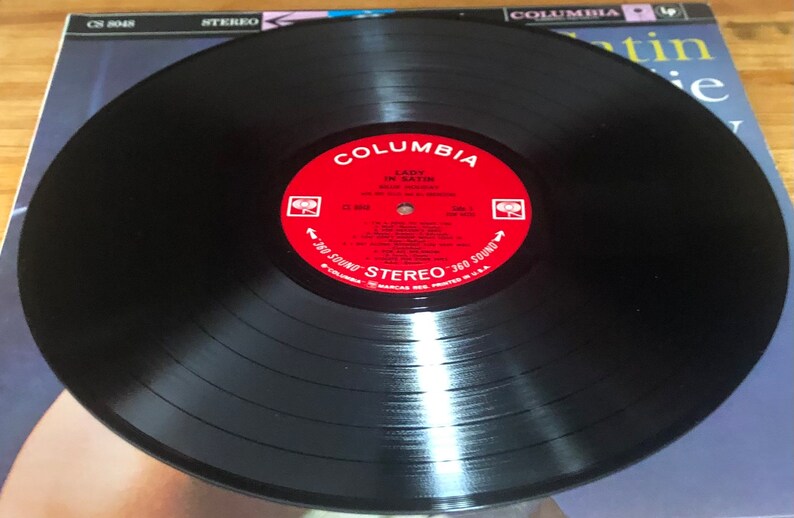 Op de afbeelding: Een zwarte vinylplaat met een rood label waarop "Columbia" en "Lady in Satin" staat met de artiest "Julie London" erop gedrukt. De plaat is in stereo-formaat en heeft een 360-geluid.