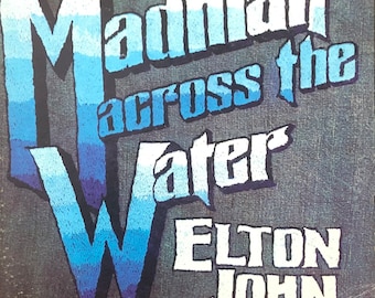 May include: A vintage vinyl record album cover with a blue and white gradient design. The album title is "Madman Across the Water" by Elton John. The record label is MCA Records.