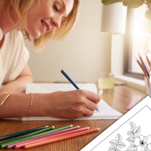 May include: A woman is coloring a black and white illustration of a rose with colored pencils. The illustration is on a white sheet of paper. The woman is sitting at a wooden table with a vase of flowers in the background.