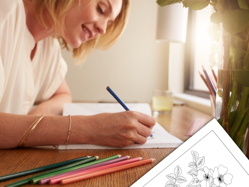 May include: A woman is coloring a black and white illustration of a rose with colored pencils. The illustration is on a white sheet of paper. The woman is sitting at a wooden table with a vase of flowers in the background.