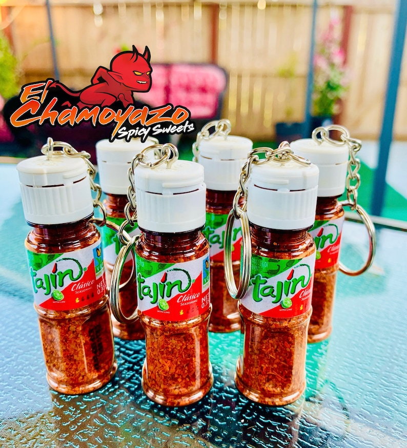 May include: Five small clear glass bottles with white lids and silver keychains. Each bottle contains red and orange Tajin seasoning and has a green and white label with the text "Tajin Clasico Seasoning" and a lime image.
