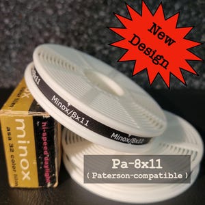 Może przedstawiać: Białe szpule do wywoływania filmu Pa-8x11 z czarnym tekstem, z napisem "Minox/8x11". Widoczne jest również pudełko filmu kolorowego Minox asa 32. Obraz zawiera czerwoną grafikę w kształcie gwiazdy z napisem "New Design".