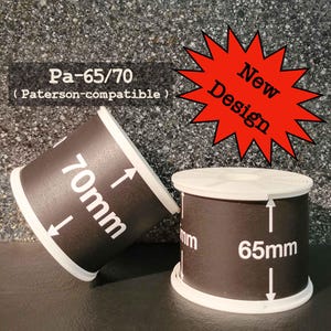 Puede incluir: Dos carretes de revelado de película en blanco y negro. Uno está etiquetado 70 mm, el otro 65 mm. El texto "Pa-65/70 (compatible con Paterson)" está arriba. Una estrella roja dice "Nuevo diseño".