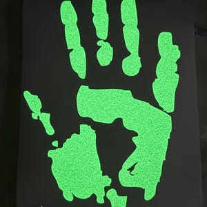 May include: A glowing green handprint on a black background. The handprint is textured and appears to be glowing. The image is a close-up of the handprint.