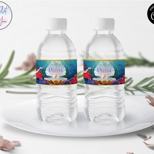 May include: Two clear water bottles with white caps, each featuring a custom label. The labels showcase a mermaid theme with a pearl, the name "Olivia", and the number "2". The design includes red, blue, and gold accents, set against a blue underwater backdrop.