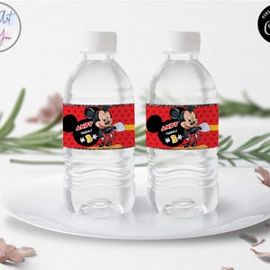 Puede incluir: Dos botellas de agua de pl&aacute;stico transparente con tapas blancas. Cada botella tiene una etiqueta roja con Mickey Mouse, el texto "ANDY TURNS 1" y una franja amarilla. Las botellas est&aacute;n sobre un plato blanco.