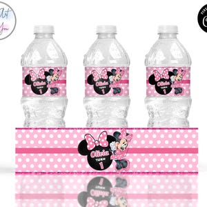 K&ouml;nnte beinhalten: Drei klare Wasserflaschen mit rosa Minnie Mouse-Themenetiketten. Jedes Etikett zeigt eine schwarze Silhouette von Minnie's Kopf mit einer rosa Schleife, den Namen "Olivia" und die Zahl "1". Ein passendes rosa gepunktetes Banner befindet sich unten.