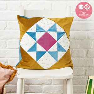 May include: A mustard yellow velvet pillow with a blue and white patchwork star design in the center. The star is made of triangles and squares. The pillow is sitting on a white chair.