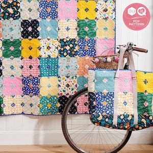 May include: A colorful patchwork quilt with a floral and geometric pattern hangs on a white wall. A bicycle with a basket and a matching patchwork tote bag are in front of the quilt.