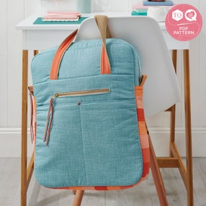 May include: A teal blue quilted tote bag with orange straps and a zippered pocket. The bag has a checkered pattern on the bottom and is hanging on a white chair.
