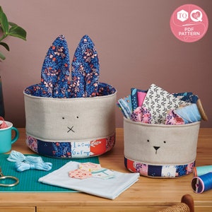 May include: Two fabric storage baskets shaped like bunnies with floral fabric ears. The baskets are made of natural linen fabric with a patchwork design around the bottom. The larger basket has the text "I'm Coming 6 in May" written on the side.