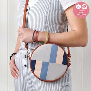 May include: A round crossbody bag made from brown leather with a patchwork design featuring blue, grey, and pink fabric squares. The bag has a gold clasp and a brown leather strap.