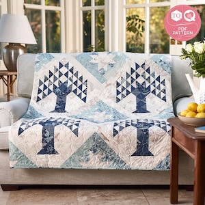 May include: A blue and white quilt featuring a tree design. The quilt is made from a variety of fabrics, including a blue and white check, a blue and white floral, and a plain blue. The quilt is shown on a sofa in a living room.
