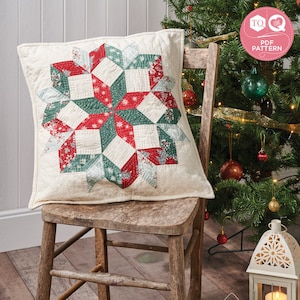 May include: A white cushion with a red and green snowflake design. The cushion is sitting on a wooden chair in front of a Christmas tree.