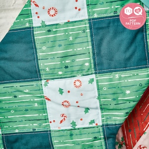 May include: A patchwork quilt featuring a green, blue and white pattern. The quilt is made up of squares with various designs, including candy canes, holly leaves and stripes. The quilt is stitched together with white thread.