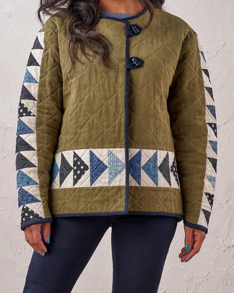 Puede incluir: Chaqueta acolchada verde oliva con detalles de patchwork geom&eacute;trico en tonos azules, blancos y negros. Presenta un patr&oacute;n de diamantes, ribete azul oscuro y cierres de palanca. Una prenda de abrigo elegante.