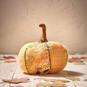 Peut inclure: Une citrouille en tissu faite &agrave; la main avec une tige marron et des motifs floraux. La citrouille est principalement jaune et orange, avec des coutures d&eacute;coratives et des feuilles. C'est un objet d&eacute;coratif sur le th&egrave;me de l'automne.