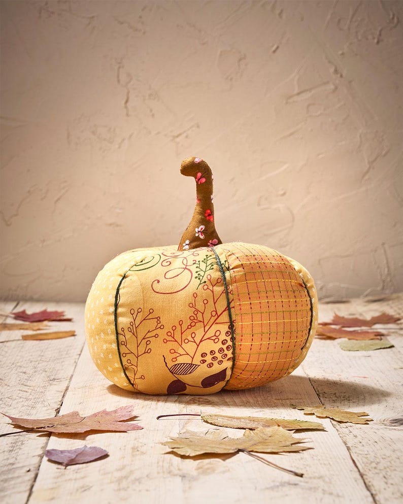 Peut inclure: Une citrouille en tissu faite &agrave; la main avec une tige marron et des motifs floraux. La citrouille est principalement jaune et orange, avec des coutures d&eacute;coratives et des feuilles. C'est un objet d&eacute;coratif sur le th&egrave;me de l'automne.