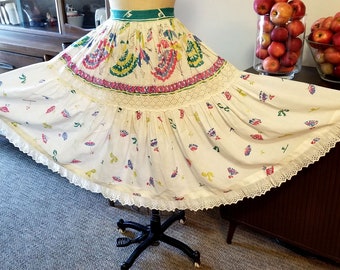 Puede incluir: Una falda de algodón blanca con estampado floral de colores y ribete de encaje. La falda tiene un diseño de capas y está fruncida en la cintura.