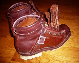 May include: A pair of brown leather hiking boots with a buckle closure and a lace-up front. The boots have a thick rubber sole and a rugged design.