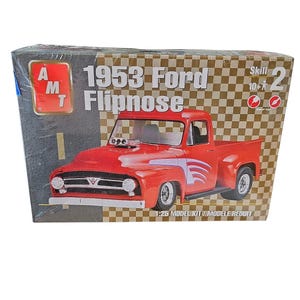 May include: A model kit box featuring a red 1953 Ford Flipnose pickup truck. The box has the text "1953 Ford Flipnose" and "1:25 Model Kit". The background is a checkered pattern.