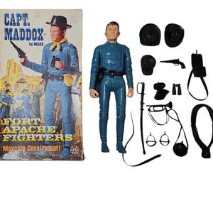 May include: A vintage Captain Maddox action figure with accessories, including a hat, gun, and saddle. The box art features a cowboy illustration with the text "Fort Apache Fighters". The figure is in a blue uniform.