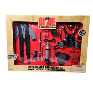 Op de afbeelding: Een G.I. Joe Classic Collection Underwater Demolition Set in een houten doos. De set bevat een zwart en grijs wetsuit, duikuitrusting, een tank en andere accessoires. De doos heeft de tekst "Underwater Demolition Set".