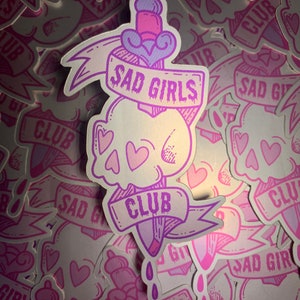 May include: A pink and purple sticker with a skull and a dagger. The dagger has a banner that says "Sad Girls Club".