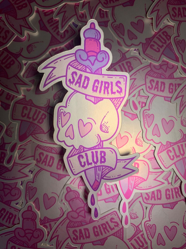 May include: A pink and purple sticker with a skull and a dagger. The dagger has a banner that says "Sad Girls Club".