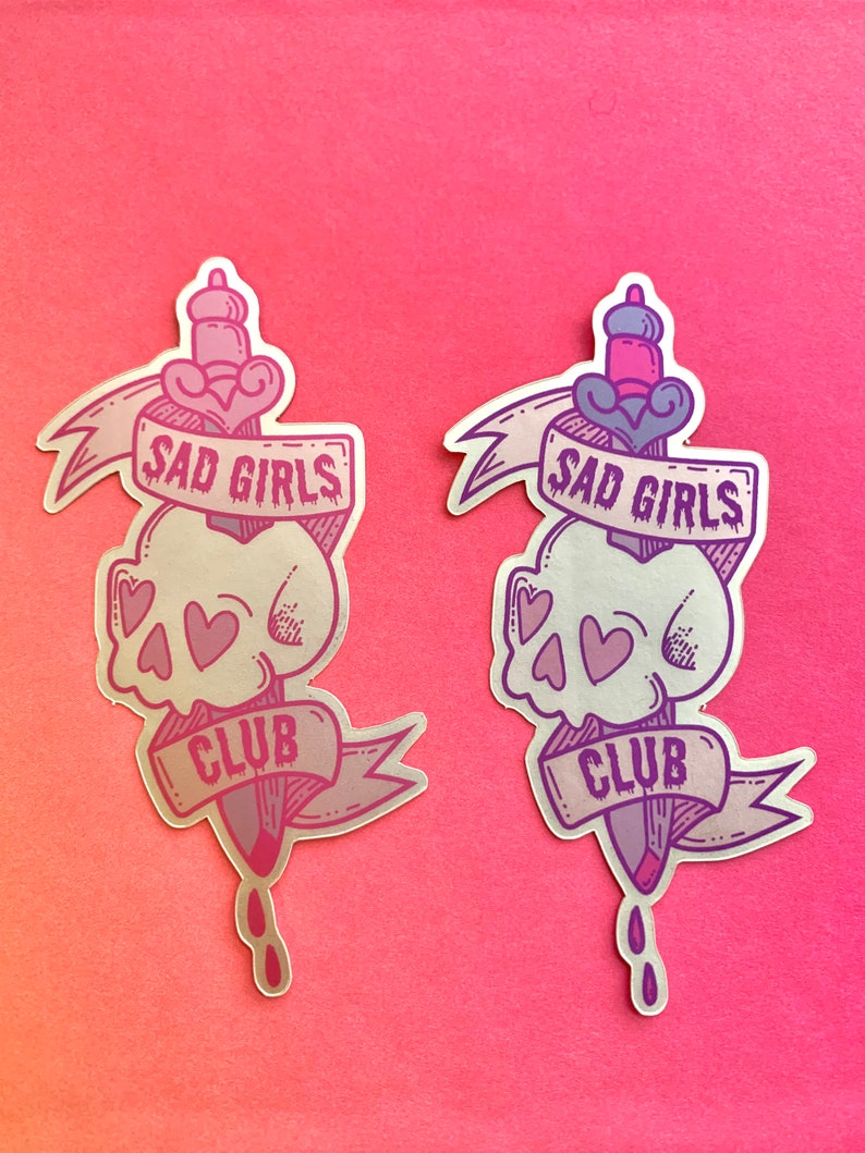 May include: Two silver holographic stickers with a skull and dagger design. The stickers feature the text "Sad Girls Club" in a purple font.