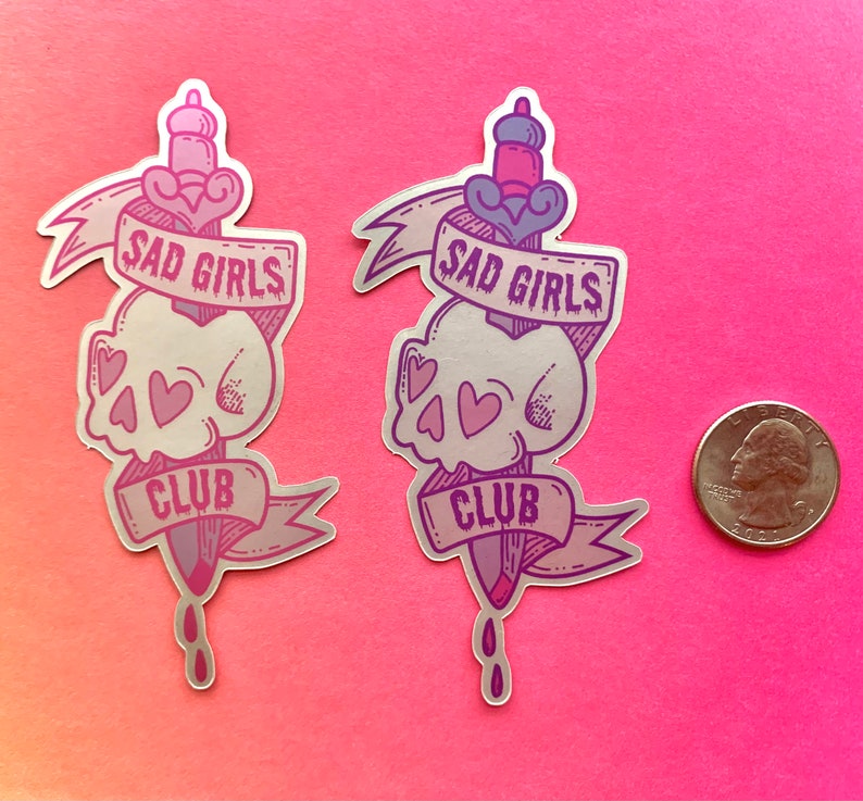 May include: Two silver holographic stickers with a skull and dagger design. The stickers feature the text "Sad Girls Club" in a pink and purple gradient.