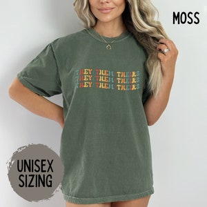 May include: A green t-shirt with the text "THEY/THEM/THEIRS" repeated three times in a rainbow font.