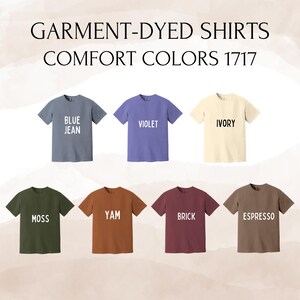 May include: A collection of eight garment-dyed t-shirts in various colors, including blue jean, violet, ivory, moss, yam, brick, and espresso. Each shirt has a crew neck and short sleeves. The text "GARMENT-DYED SHIRTS COMFORT COLORS 1717" is at the top.