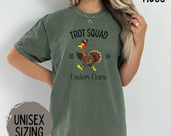 May include: Moss green unisex t-shirt with the text "Trot Squad 2024" and a cartoon turkey graphic. The shirt also has the words "Custom Name" printed below the turkey. The shirt is a unisex size.