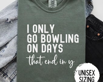 May include: A green t-shirt with the text "I only go bowling on days that end in y" in white. The shirt has a unisex sizing label.