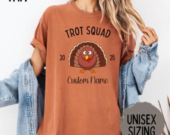 May include: Rust-colored t-shirt with a turkey graphic and the text "Trot Squad" above and "Custom Name" below. The turkey has a brown body, a red wattle, and a fan of brown and tan feathers. The shirt also has the text "20 25" on either side of the turkey.
