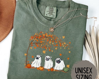 May include: A green t-shirt with a print of three pugs dressed as ghosts in front of a tree with autumn leaves. The text "MOSS" is in the top right corner of the image. The text "UNISEX SIZING" is in the bottom right corner of the image.