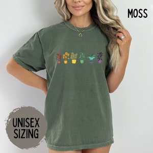 May include: A green unisex t-shirt with a rainbow row of potted plants. The text "MOSS" is in the top right corner of the image. The text "UNISEX SIZING" is in the bottom left corner of the image.