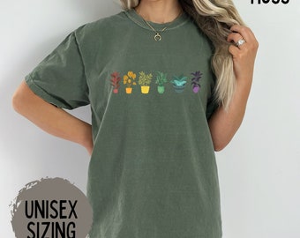 Puede incluir: Una camiseta unisex verde con una fila arcoíris de plantas en macetas. El texto "MOSS" está en la esquina superior derecha de la imagen. El texto "UNISEX SIZING" está en la esquina inferior izquierda de la imagen.