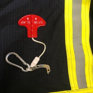 May include: A red safety device with a pull tab and a hook. The device has the words "Jerk to Inflate" printed on it.