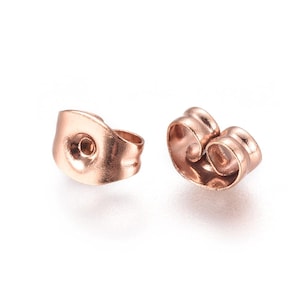 May include: Two rose gold earring backs, also known as butterfly backs, are shown against a white background. The earring backs are made of metal and have a curved design. One back is viewed from the front, and the other is viewed from the side.