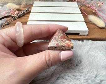 May include: A small, triangular, pink and brown, polished, pyramid-shaped crystal.