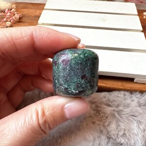 May include: A tumbled green and red gemstone with a smooth, rounded surface. The stone has a mottled appearance with green and red hues.