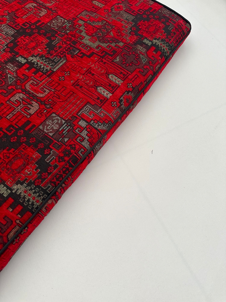 Puede incluir: Un coj&iacute;n rojo y negro con estampado y borde negro. El coj&iacute;n est&aacute; hecho de una tela suave y texturizada.