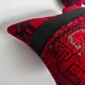May include: Two red throw pillows with black and gold patterned fabric. The pillows have black elastic bands around the edges.