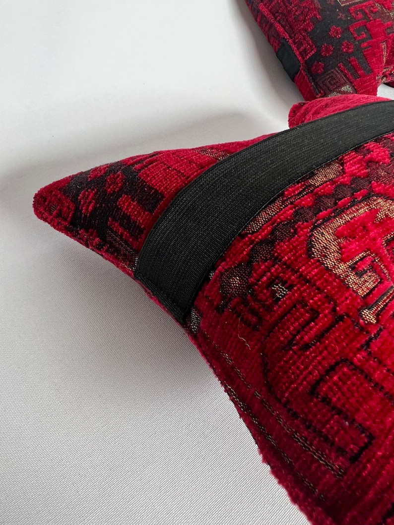 May include: Two red throw pillows with black and gold patterned fabric. The pillows have black elastic bands around the edges.